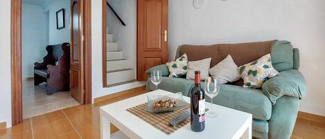 A living room with a green sofa, a white coffee table, and a bottle of wine.