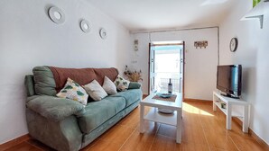 A living room with a green sofa, a coffee table, a TV on a stand, and a balcony with a view. - 2 bedroom gorgeous home in Algodonales (Algodonales)