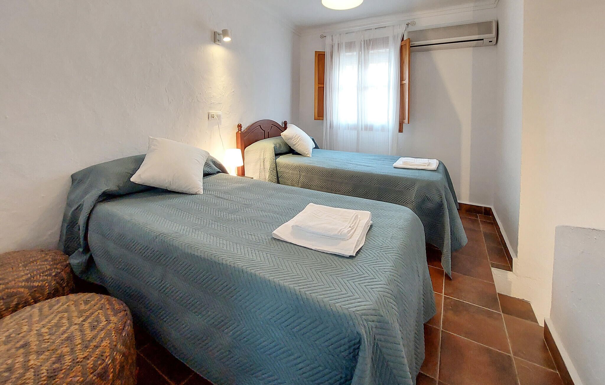 A hotel room with two beds, a wall-mounted air conditioner, and a window with curtains.