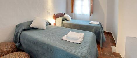 A hotel room with two beds, a wall-mounted air conditioner, and a window with curtains.
