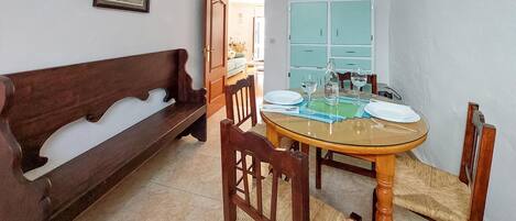 Un comedor con una mesa redonda de vidrio, sillas de madera, un banco de madera y un armario azul claro.
