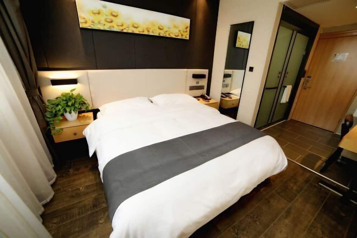 A neatly made bed with a white and gray bedspread, a bedside table with a lamp, and a potted plant.