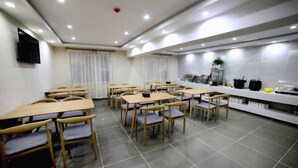 Un espace repas comprenant plusieurs tables et chaises, un long comptoir équipé d’appareils de cuisine et un téléviseur fixé au mur.