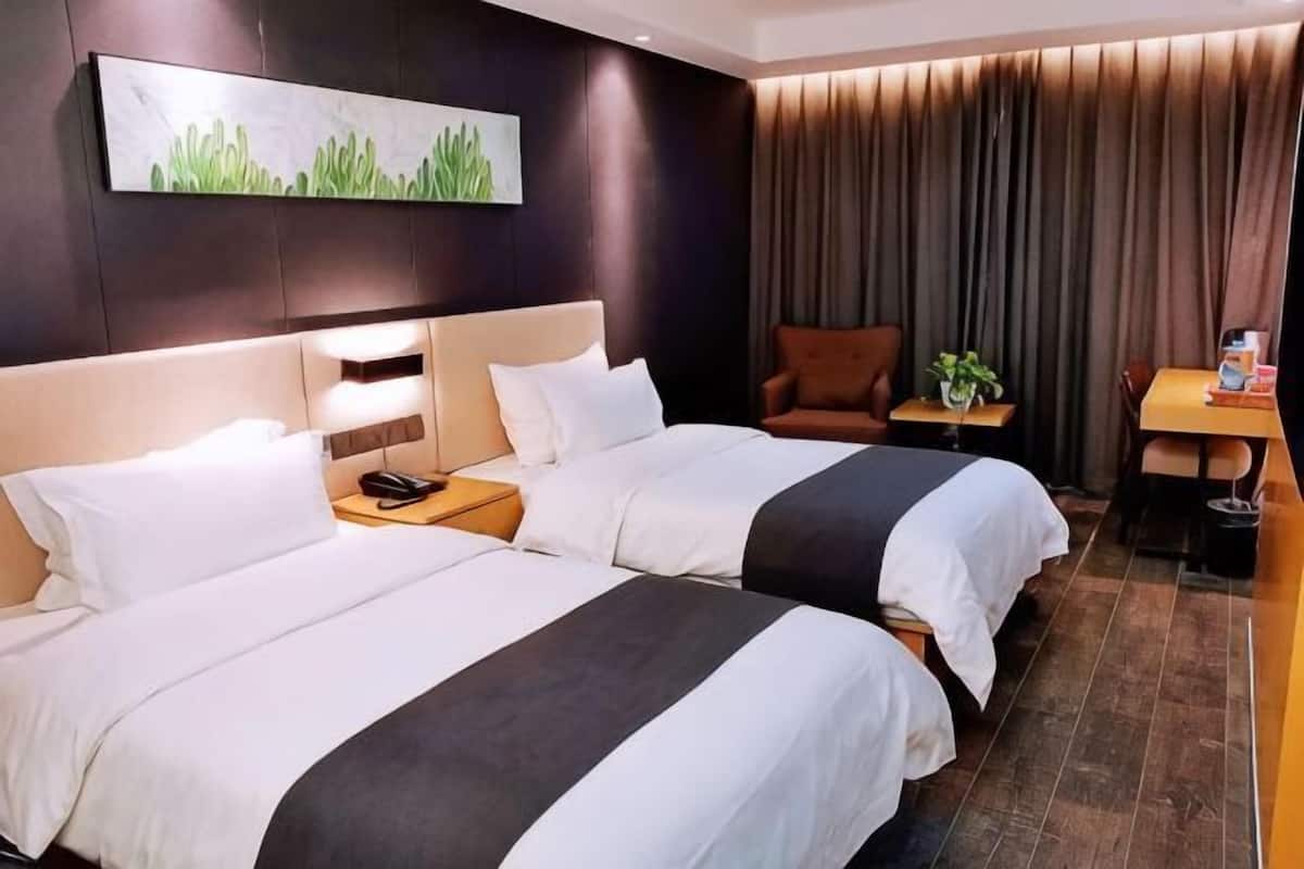 A hotel room with two beds, a small table, a chair, a plant, and a painting on the wall.