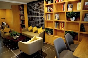 Una sala de estar moderna con un sofá, sillones, una mesa de centro y una estantería llena de libros y objetos decorativos.