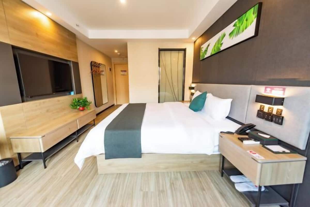 A modern hotel room with a bed, bedside table, TV, and a desk with a chair.