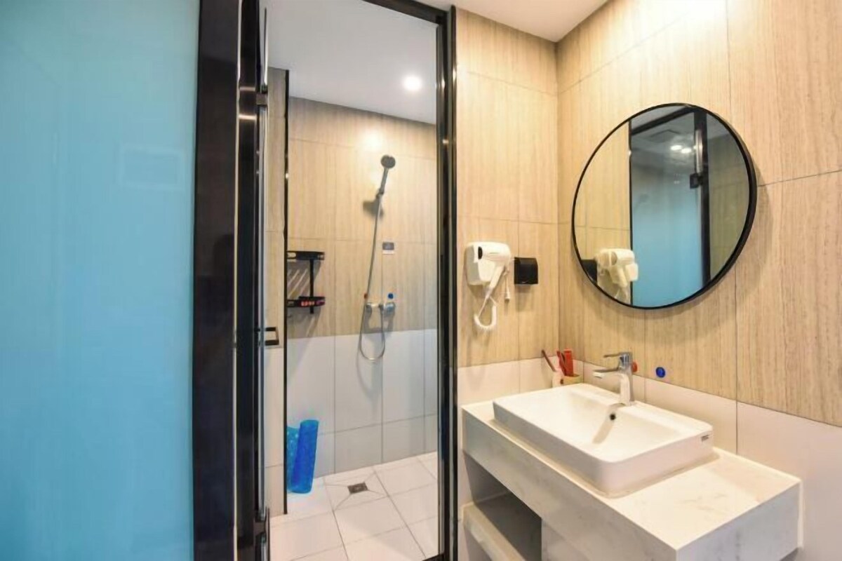 A modern bathroom with a glass shower enclosure, a white sink, and a round mirror.
