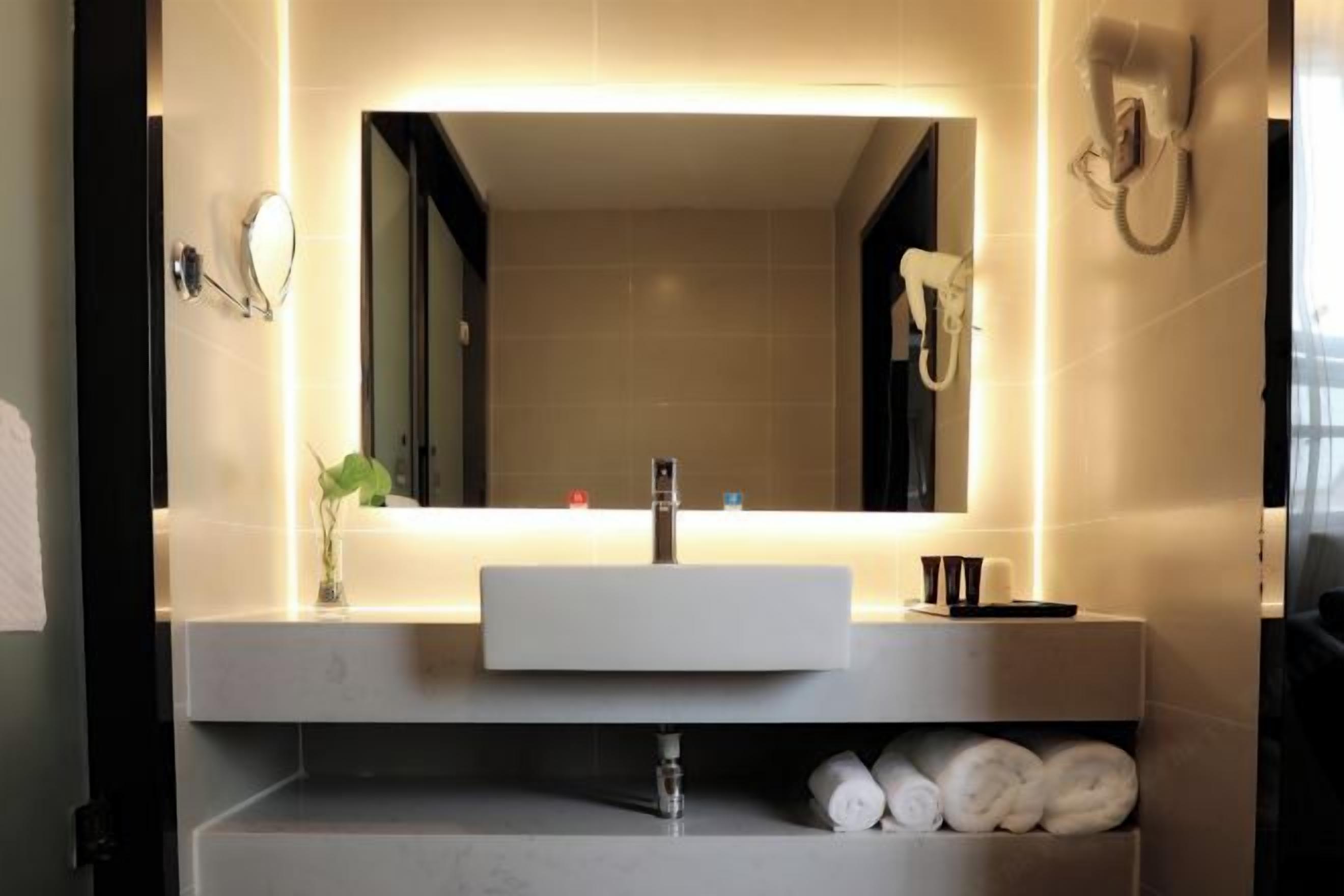 A modern bathroom with a large mirror, a white sink, and a towel rack.