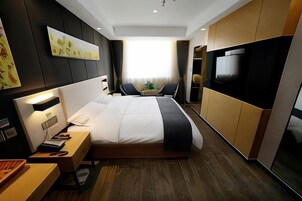 Habitación de hotel moderna con una cama grande, mesita de noche, lámpara y televisión de pantalla plana.