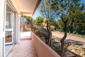 A balcony with a stone wall, a tree, and a view of a building.