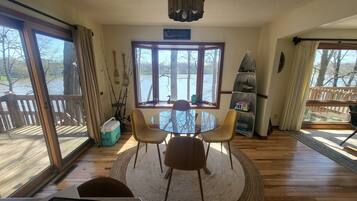 Une pièce avec une table ronde en verre, deux chaises, un petit tapis, une fenêtre donnant sur des arbres et une étagère avec des objets décoratifs.