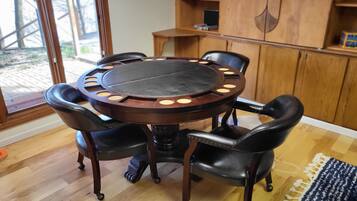 A round wooden table with six chairs, a wooden cabinet, and a view of the outdoors through a glass door.