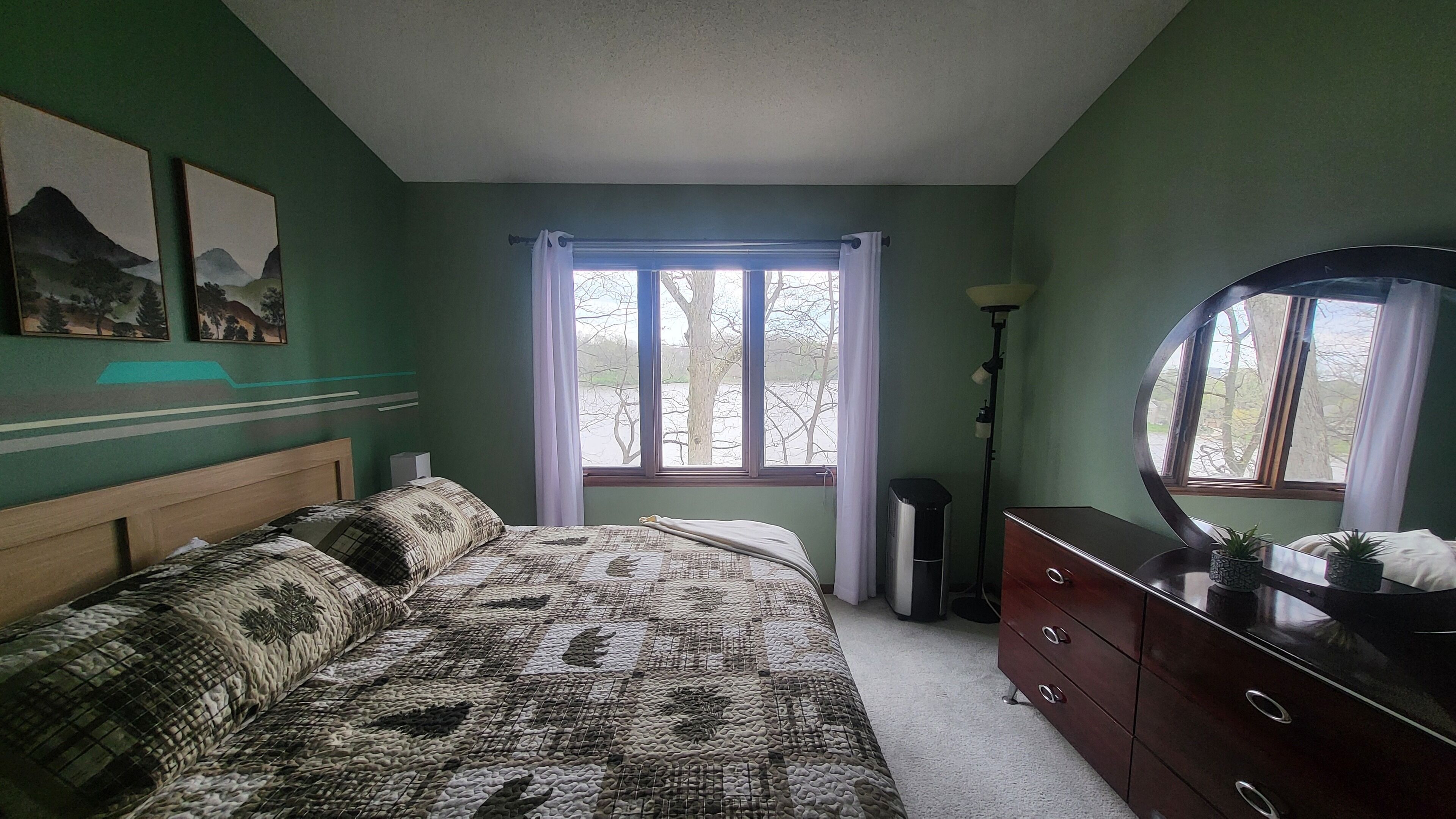 Une chambre à coucher avec un lit, une commode et une fenêtre donnant sur des arbres.
