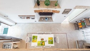 A high-ceilinged room with a stone fireplace, a dining table with chairs, and a kitchen area with a stove.