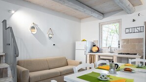 A modern kitchen with white appliances, a dining table set with green placemats, and a beige sofa.