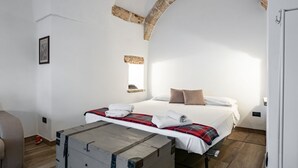 A bedroom with a bed, a wooden chest, a stone arch, and a small shelf with a picture. - GuestHost - Palazzo Rolli - The Room of the Barrels (Galatone)