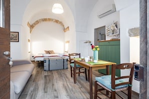 Una habitación acogedora con cama, una mesa de comedor con sillas, una pequeña cocina y un arco de piedra.