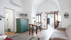A room with a sofa, a dining table with chairs, a green cabinet, and an air conditioning unit. - GuestHost - Palazzo Rolli - The Room of the Barrels (Galatone)