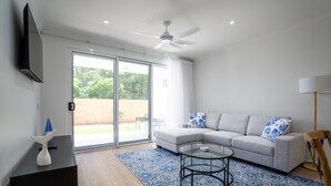 Una sala de estar moderna con un sofá modular, una mesa de centro de vidrio, una mesita auxiliar negra, un ventilador de techo y un puertas correderas de vidrio que dan a un patio.
