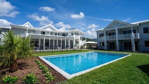 Una casa grande y moderna con piscina, varios balcones y un césped cuidado.