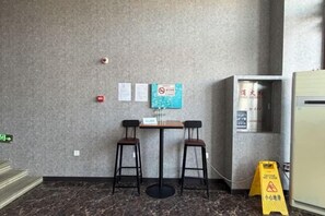 A small room with a marble floor, two chairs, a table, a vending machine, and a fire alarm on the wall. - Daqing fashion impression Theme Hotel (Daqing)