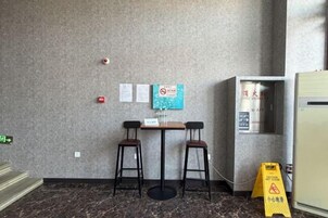 A small room with a marble floor, two chairs, a table, a vending machine, and a fire alarm on the wall.