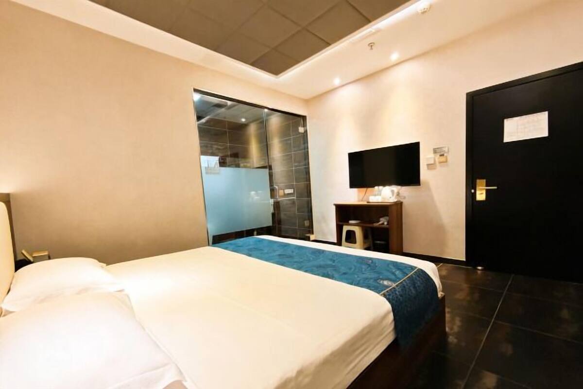 A hotel room with a bed, a TV, a mirror, and a door.