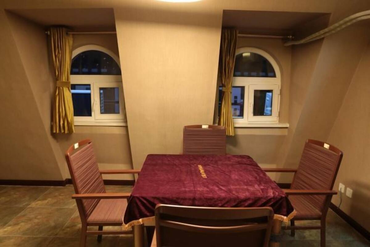 A conference room with a table and four chairs, two windows with curtains, and a tiled floor.