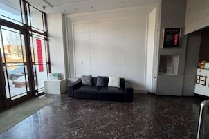 Un vestíbulo moderno con un sofá de cuero negro, una pared blanca grande y una pantalla digital.