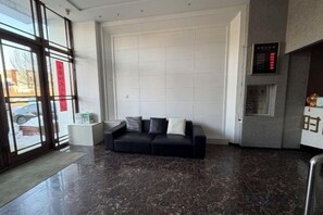 Un vestíbulo moderno con un sofá de cuero negro, una pared blanca grande y una pantalla digital.