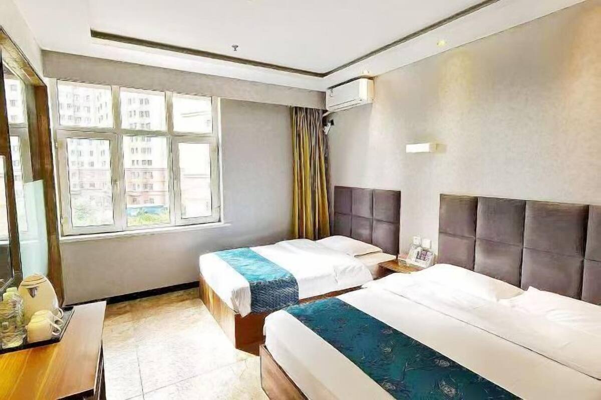 A hotel room with two beds, a window, an air conditioning unit, and a bedside table.