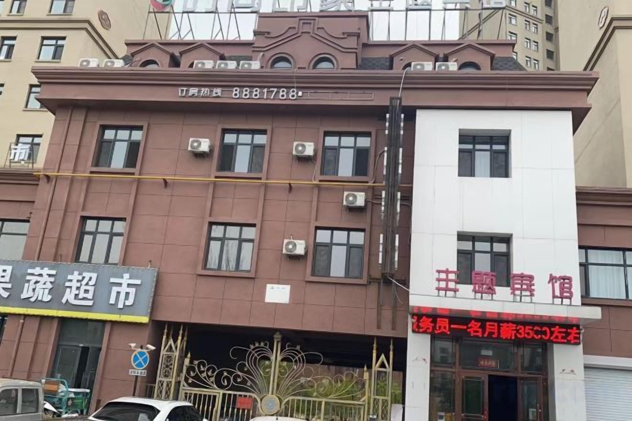 Edifício de vários andares com fachada marrom, aparelhos de ar condicionado e uma placa com texto vermelho.