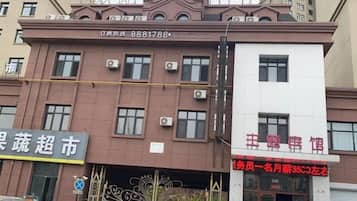 A multi-story building with a brown facade, air conditioning units, and a sign with red text.