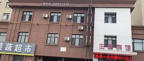 Un edificio de varios pisos con fachada marrón, unidades de aire acondicionado y un letrero con texto rojo.