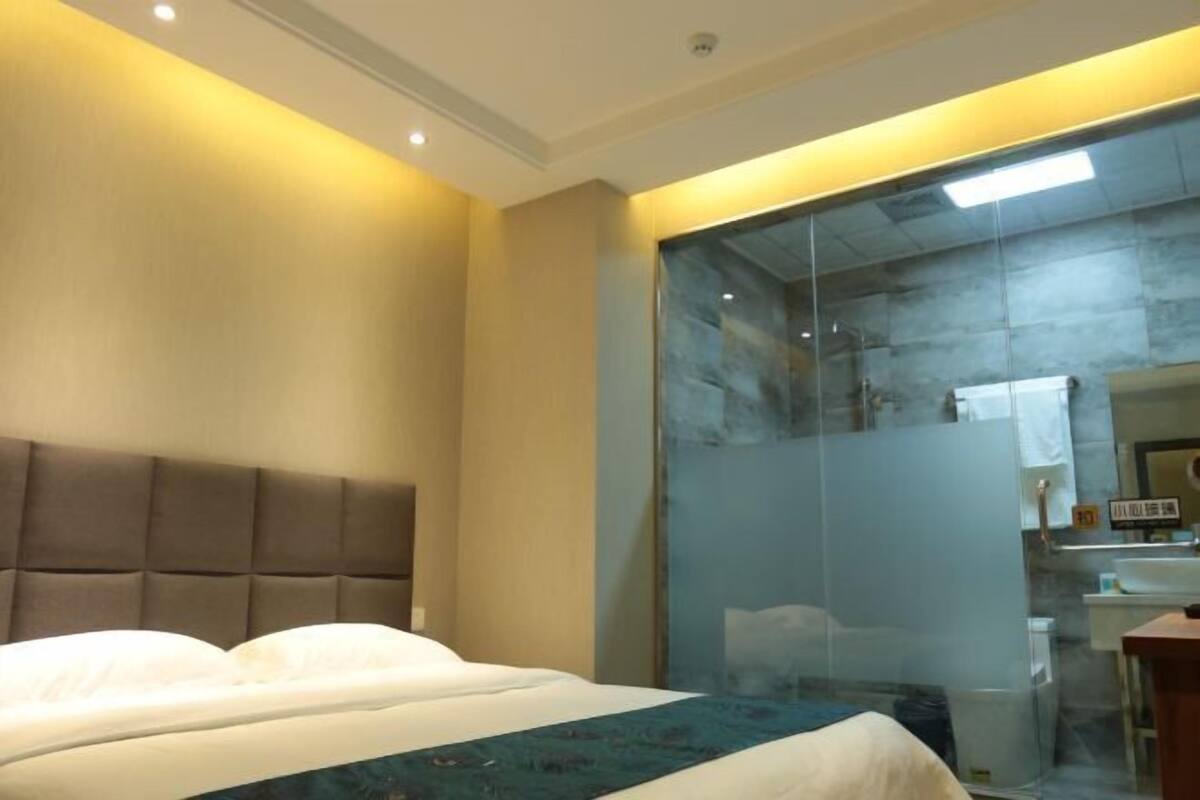 A hotel room with a bed, a glass partition, and a visible bathroom area.