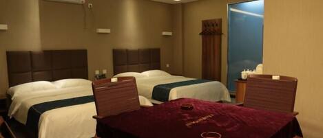 A hotel room with two beds, a table with a red tablecloth, and a window with a view.