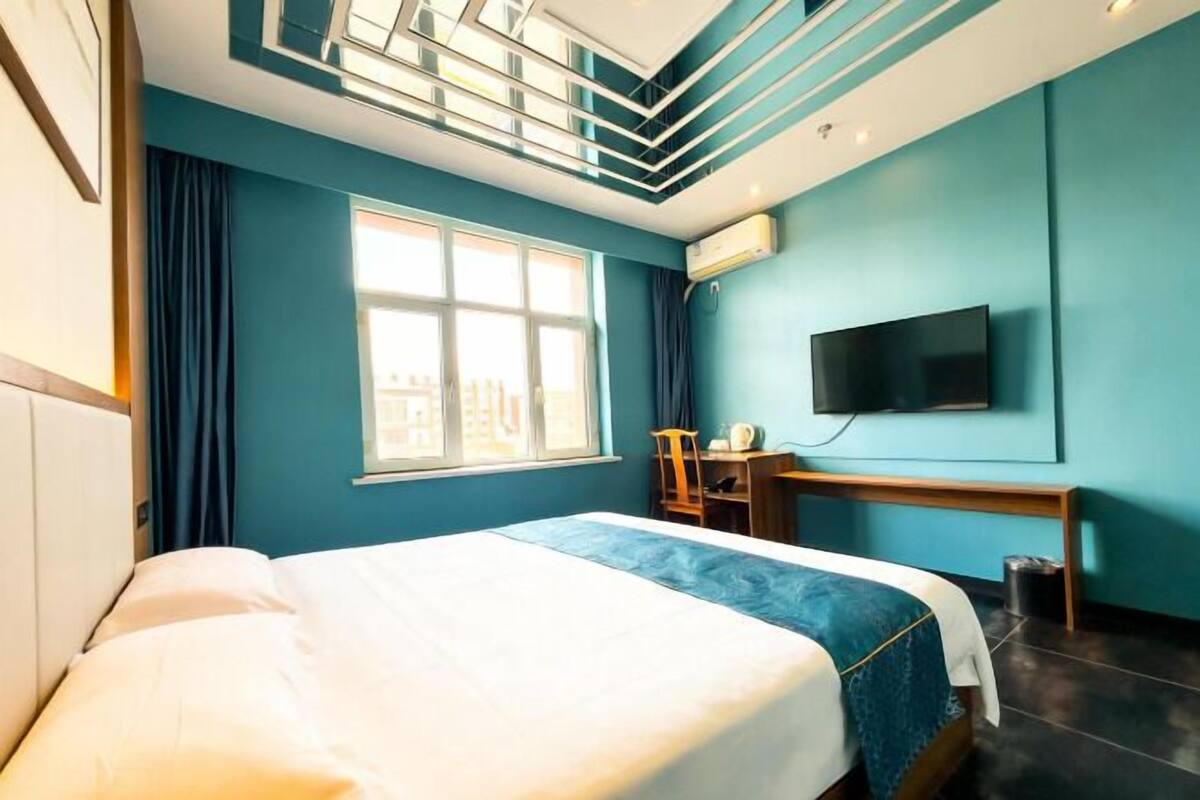 A hotel room with a bed, a desk, a chair, a TV, and a window with curtains.