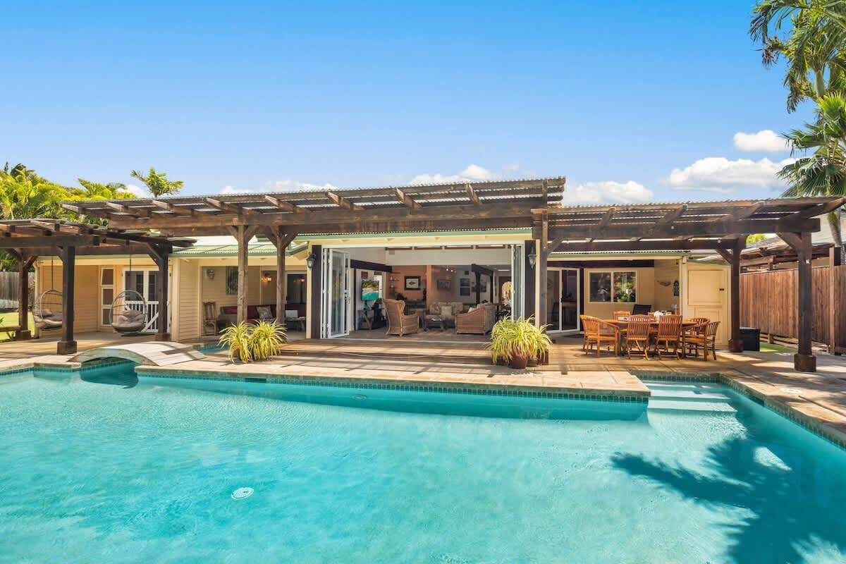 A backyard with a swimming pool, patio furniture, and a covered seating area.
