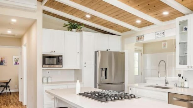 Une cuisine moderne avec des meubles blancs, des appareils électroménagers en acier inoxydable et un plafond en bois.
