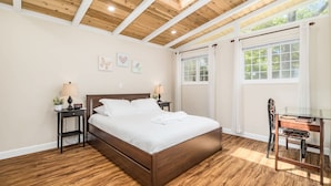 Une chambre avec un plafond en bois, un lit recouvert de draps blancs, deux tables de chevet avec des lampes et un bureau avec une chaise.