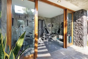 A modern gym with exercise equipment, glass doors, and a stone wall.