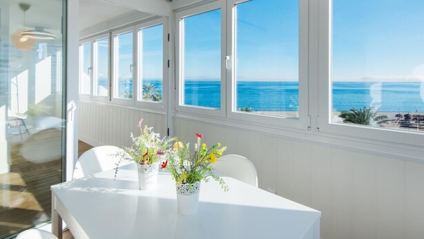 A modern room with large windows overlooking the sea, a white table with floral centerpieces, and a wicker ceiling light. - Magic of the ocean, Front Line Beach Apartment (TORREMOLINOS)