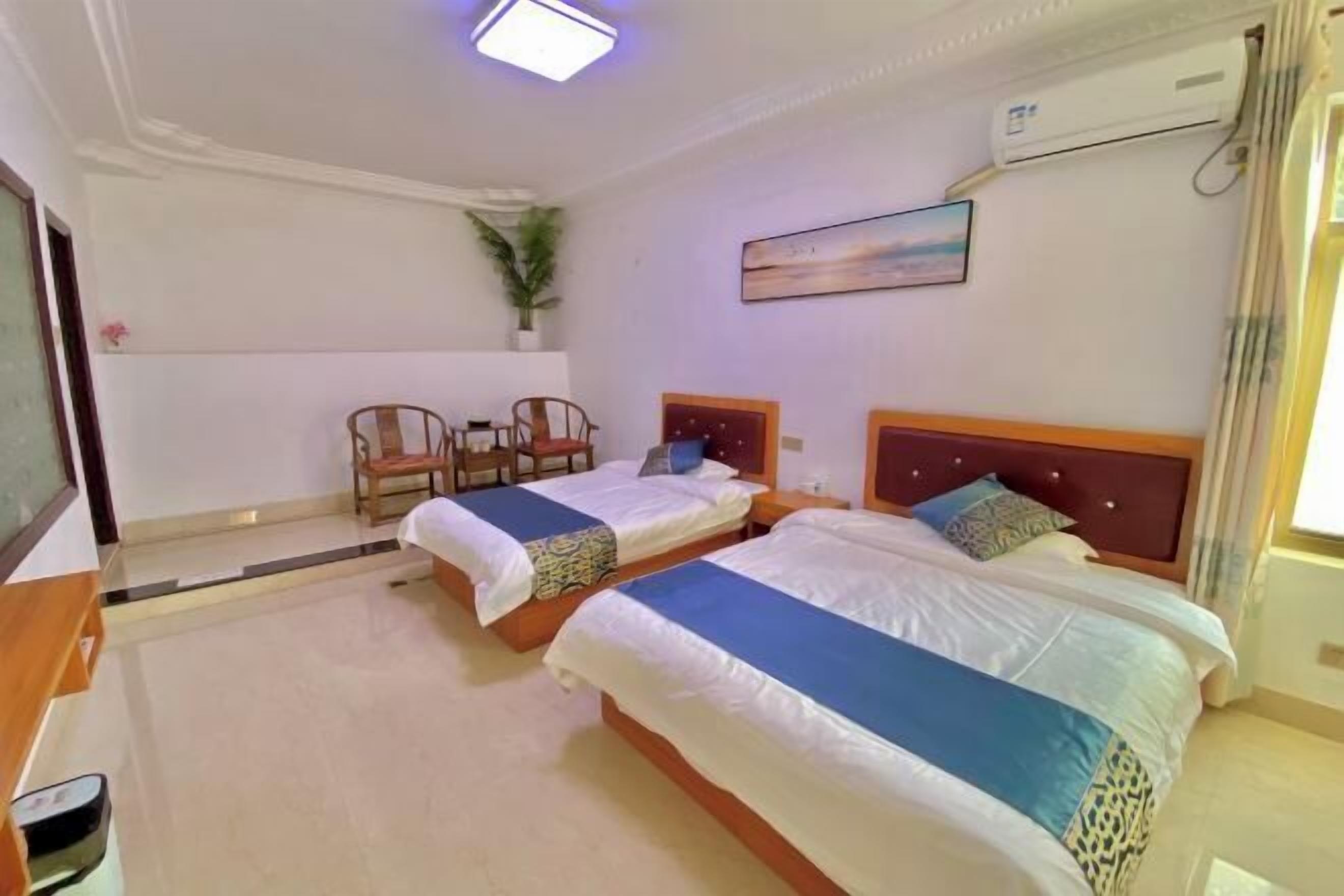 A hotel room with two beds, a desk, a chair, and a potted plant.