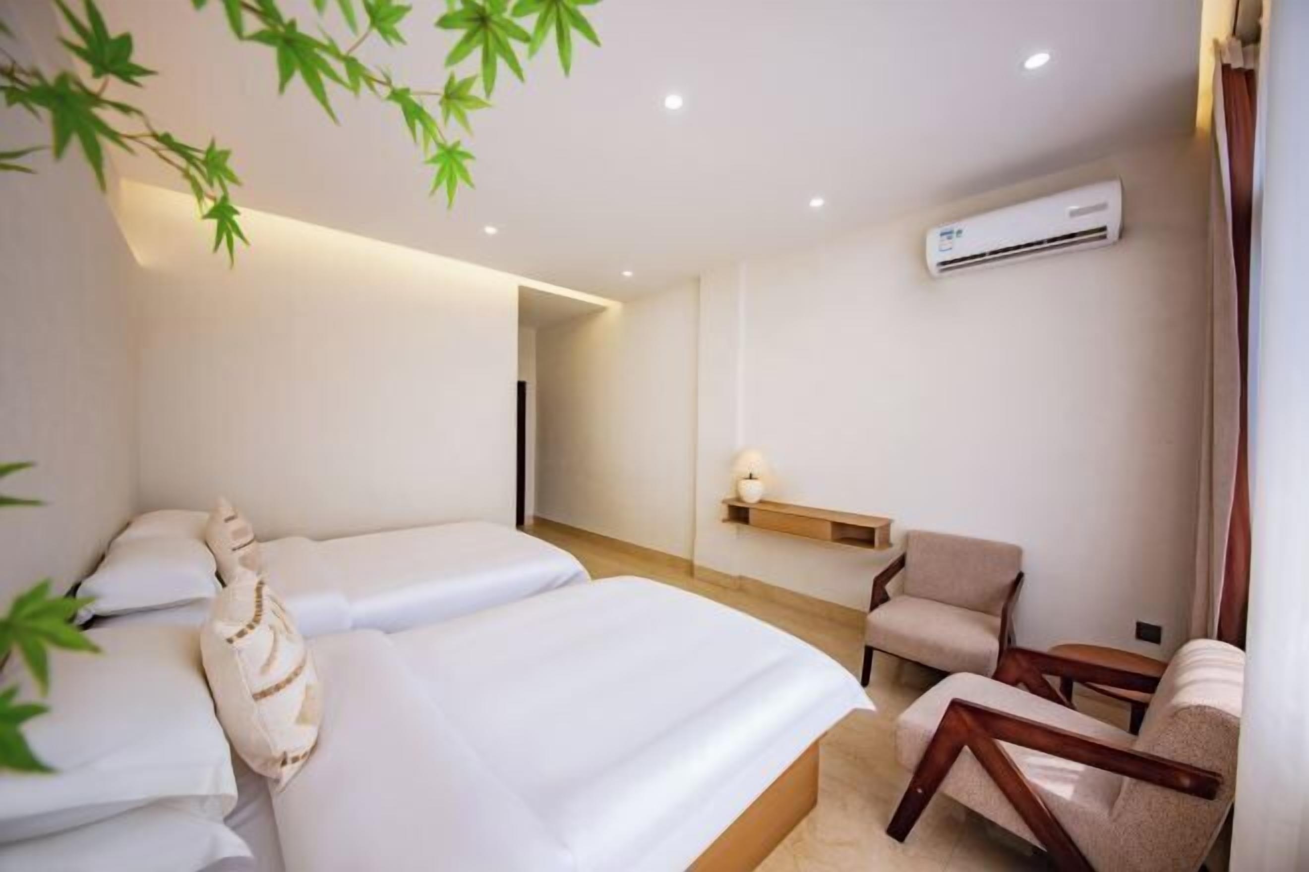 Habitación de hotel con dos camas, una zona de estar con sillas, una mesita y un equipo de aire acondicionado.