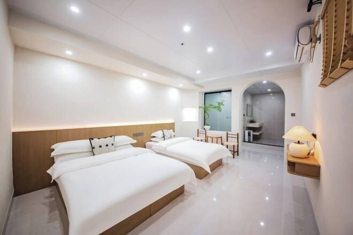 Habitación de hotel con dos camas, un escritorio, una silla, una lámpara y una planta pequeña.