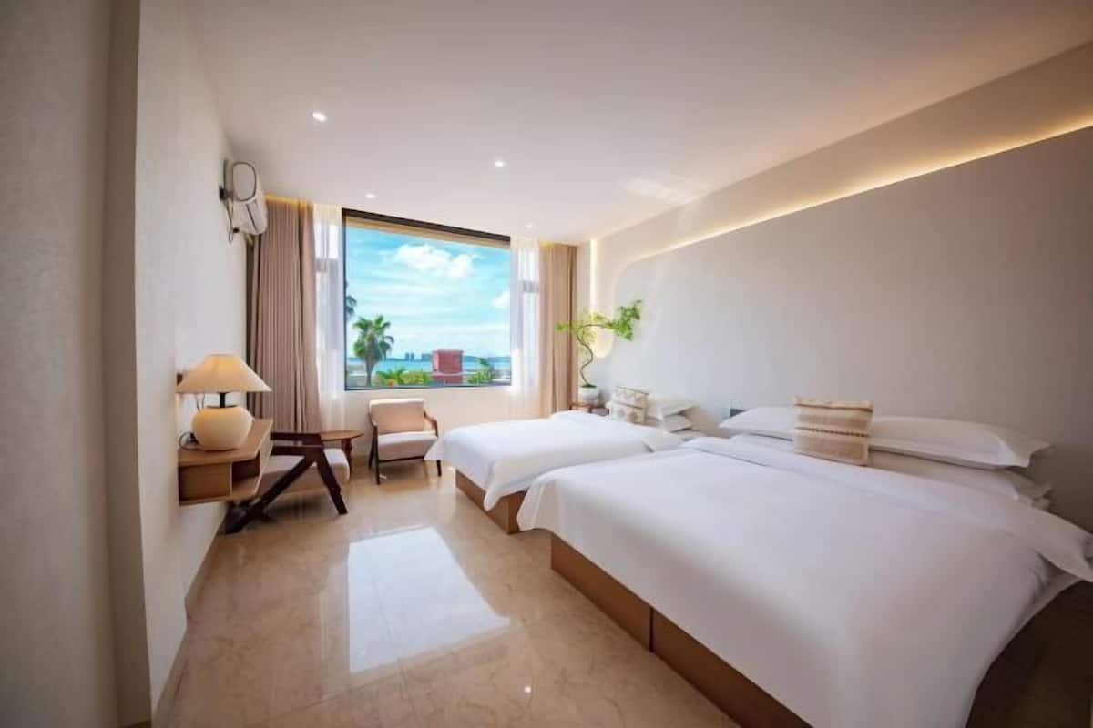 Habitación de hotel con dos camas, un escritorio, una silla, una lámpara y un ventanal con vistas.