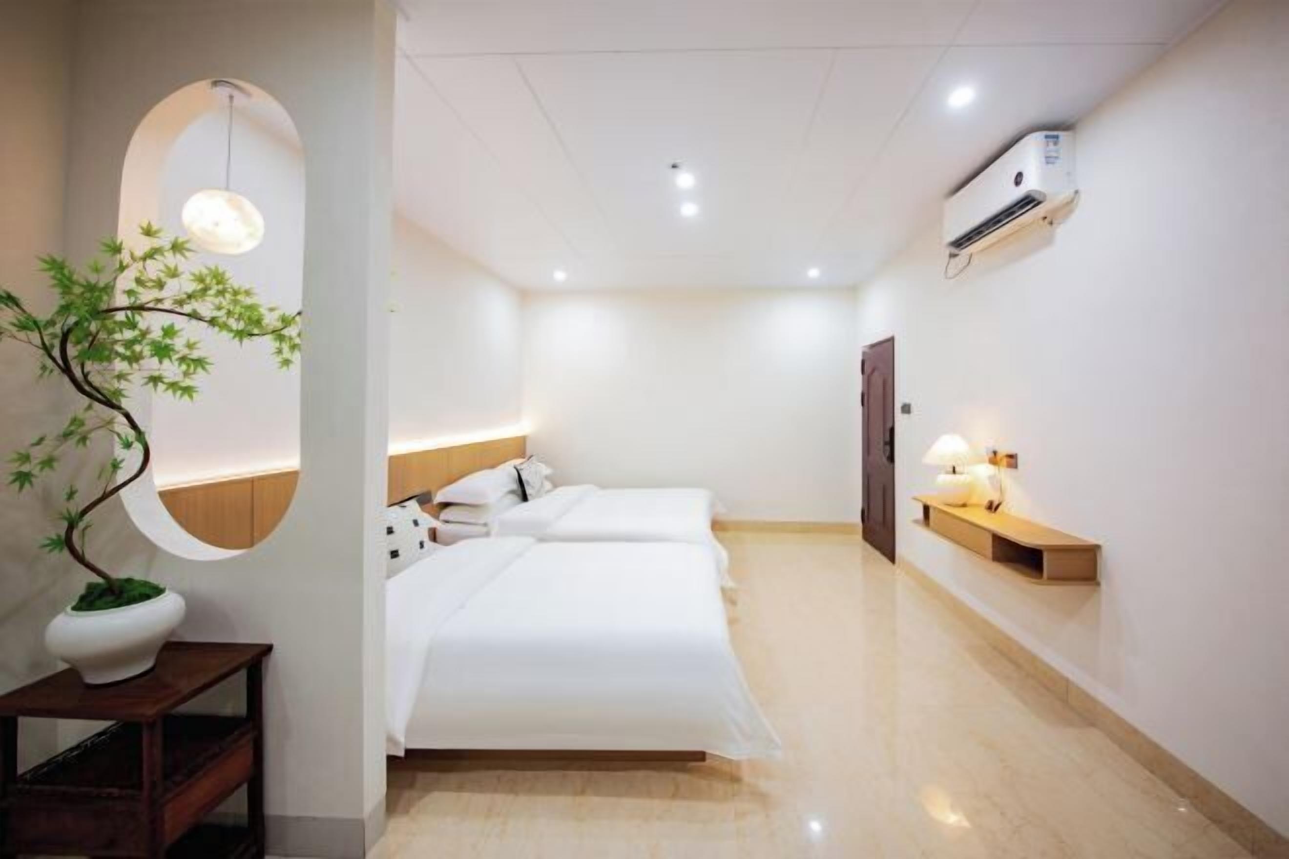 Ein Hotelzimmer mit Bett, Nachttisch, Lampe und einem Blumentopf.