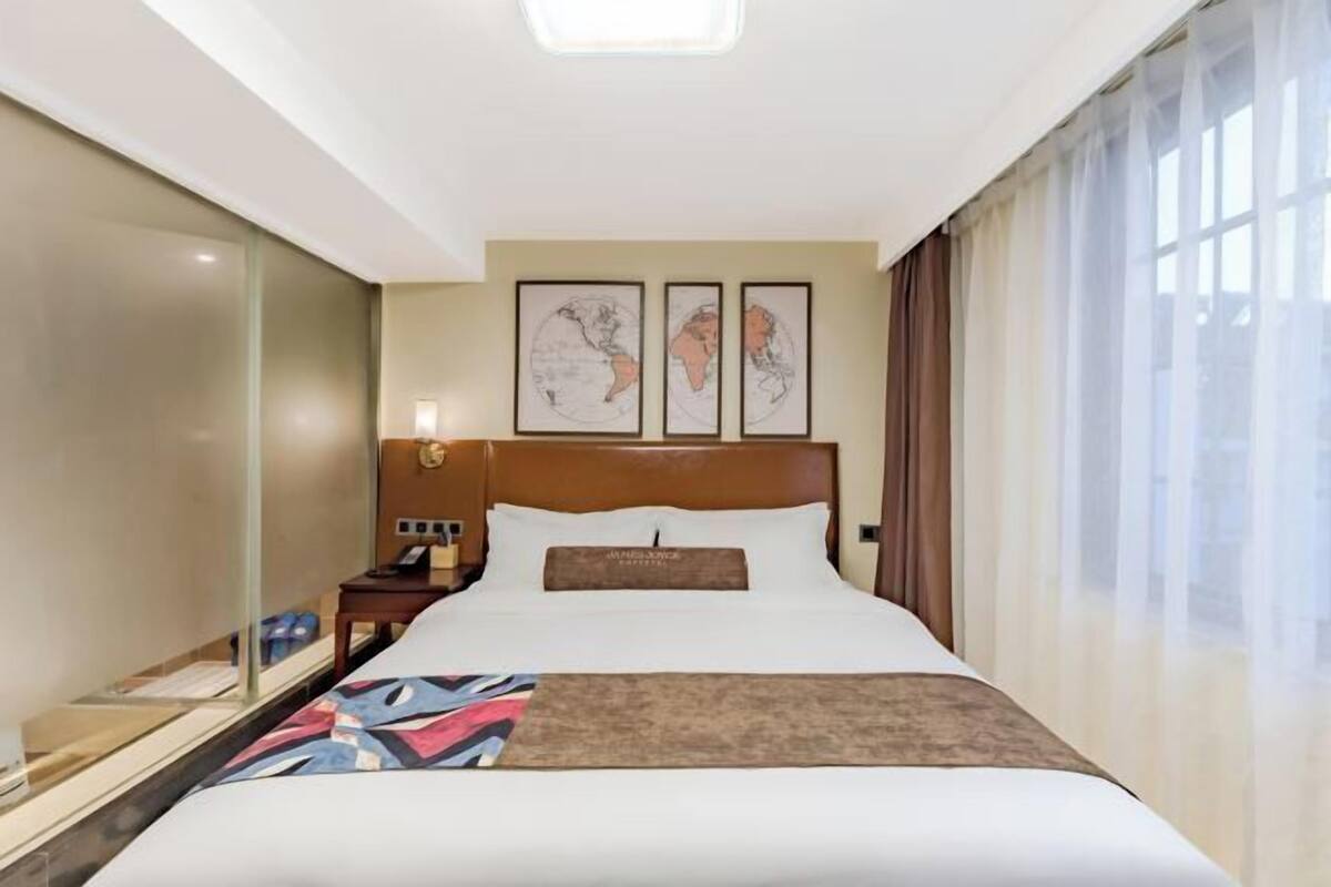 Quarto de hotel com uma cama grande, mesa de cabeceira, abajur e janela com cortinas.