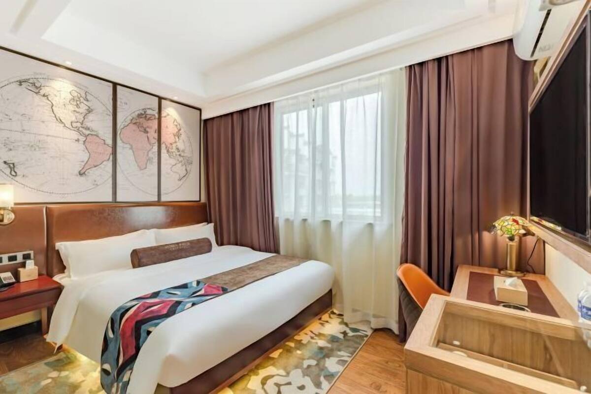 Quarto de hotel com uma cama grande, uma mesa, uma cadeira, um mapa na parede e uma janela com cortinas.