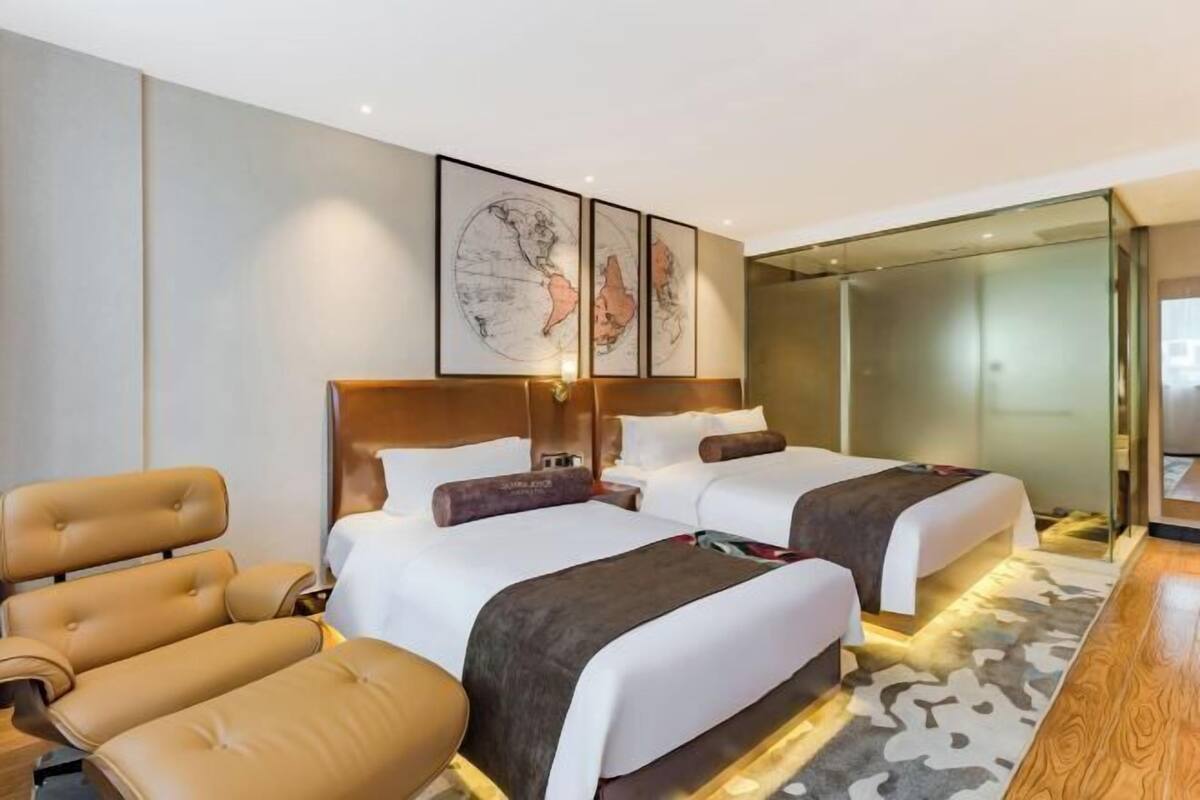 Quarto de hotel moderno com duas camas, um sofá, um painel de vidro e uma obra de arte com um mapa-múndi na parede.